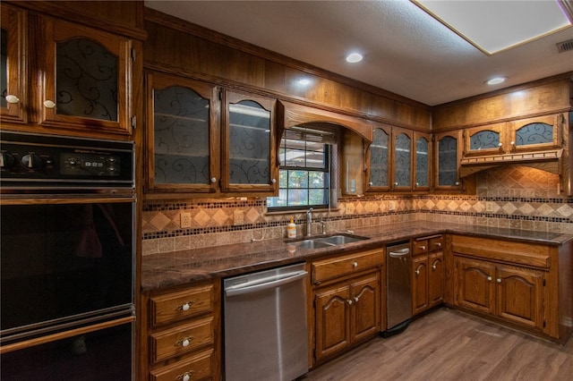 kitchen featuring dishwasher, sink, tasteful backsplash, light hardwood / wood-style flooring, and black double oven