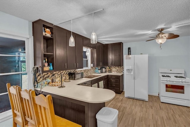 kitchen featuring dark brown cabinetry, kitchen peninsula, decorative light fixtures, white appliances, and light wood-type flooring