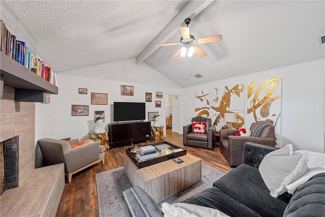 living room featuring lofted ceiling with beams, hardwood / wood-style flooring, ceiling fan, and a tiled fireplace