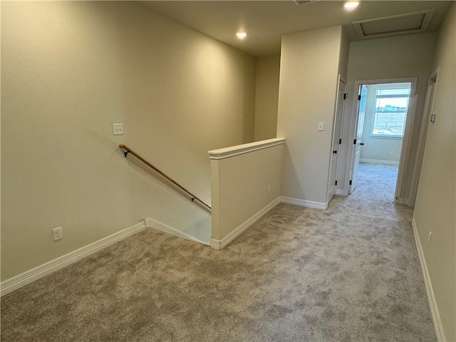 hallway featuring light carpet, attic access, baseboards, and an upstairs landing