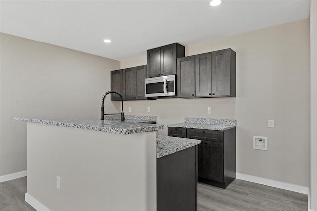 kitchen featuring sink, a center island, light stone countertops, dark brown cabinets, and light hardwood / wood-style flooring