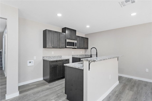 kitchen featuring sink, a breakfast bar, light stone countertops, a center island with sink, and light wood-type flooring