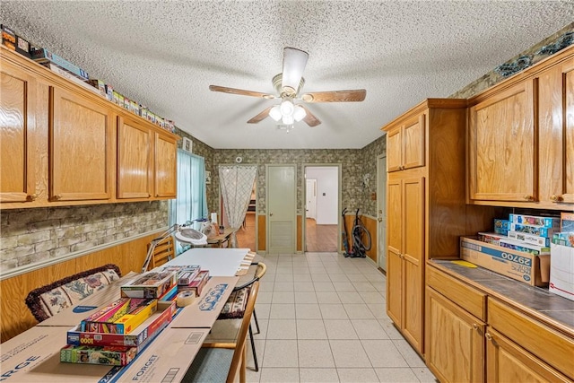 kitchen featuring ceiling fan, wood walls, light tile patterned flooring, and a textured ceiling