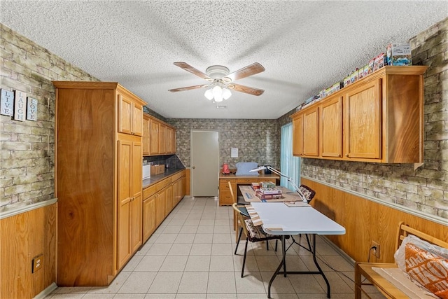 kitchen with ceiling fan, wood walls, light tile patterned floors, and a textured ceiling