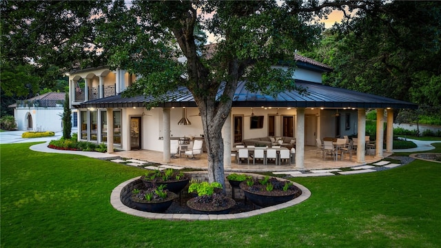 back house at dusk featuring a lawn, an outdoor living space, and a patio