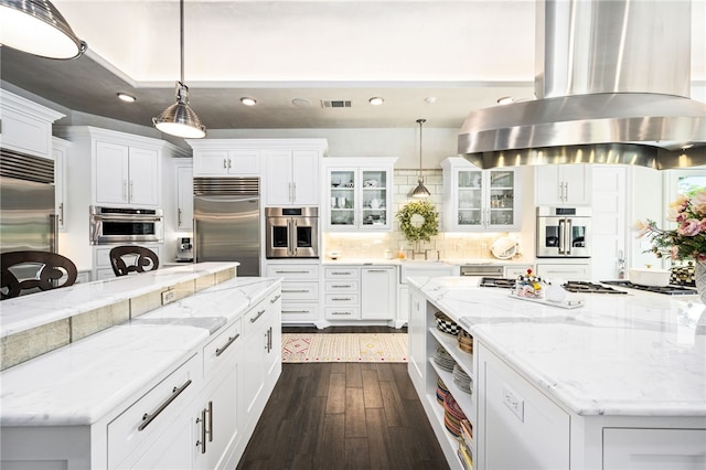 kitchen featuring built in fridge, pendant lighting, wall chimney range hood, and white cabinetry