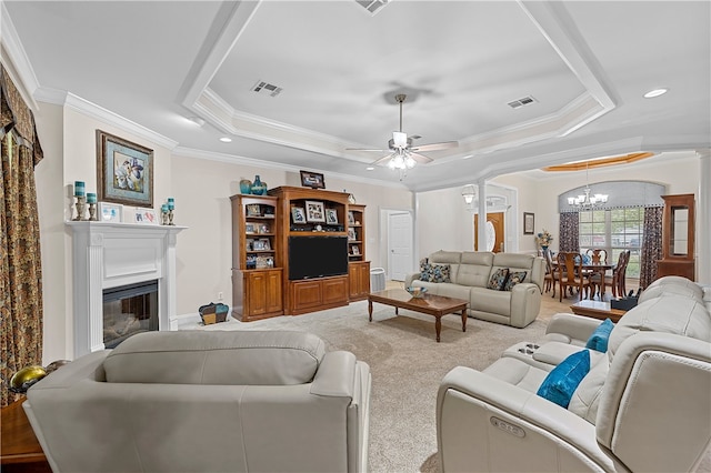 living room with a tray ceiling, crown molding, light carpet, and ceiling fan with notable chandelier