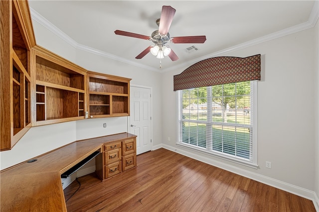 unfurnished office with built in desk, hardwood / wood-style flooring, ceiling fan, and ornamental molding