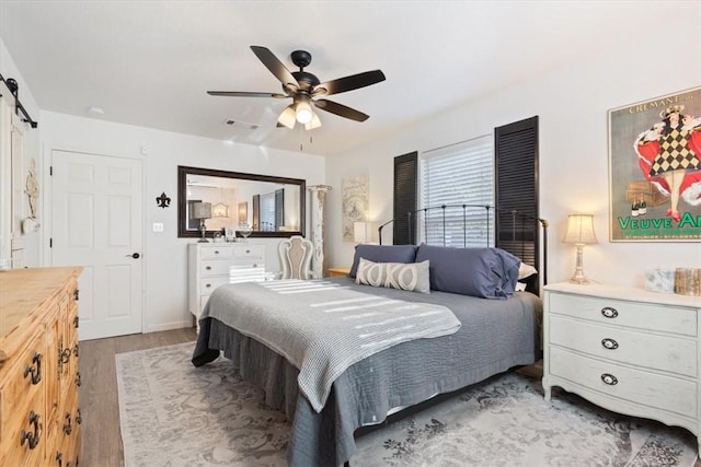 bedroom featuring a barn door, ceiling fan, and light wood-type flooring