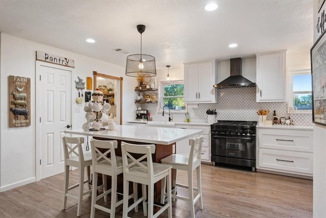 kitchen with high end range, a wealth of natural light, wall chimney exhaust hood, white cabinets, and hanging light fixtures