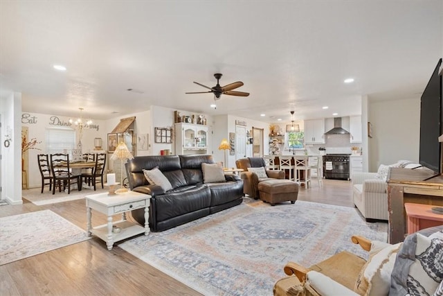 living room with ceiling fan with notable chandelier and light hardwood / wood-style flooring