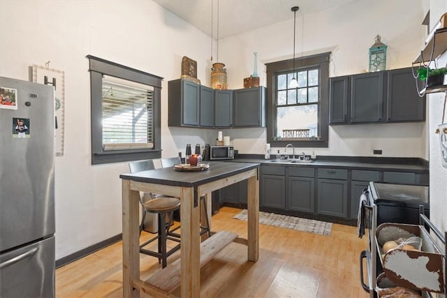 kitchen with gray cabinetry, sink, hanging light fixtures, light hardwood / wood-style floors, and stainless steel appliances