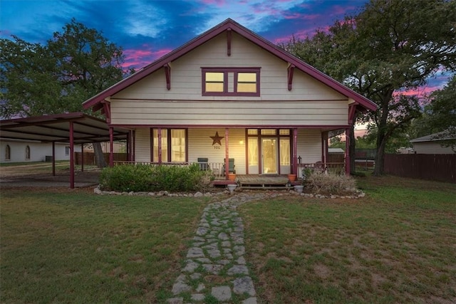 back house at dusk featuring a yard, covered porch, and a carport