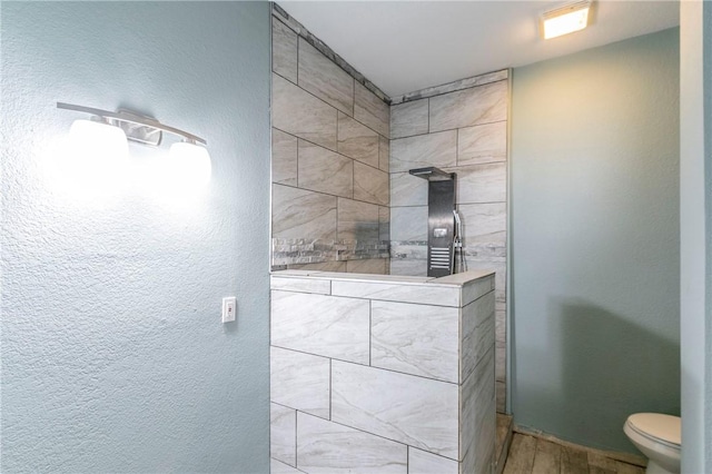 bathroom with a tile shower, toilet, and wood-type flooring