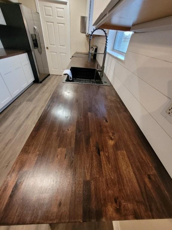 details with stainless steel refrigerator with ice dispenser, wood-type flooring, sink, and white cabinets