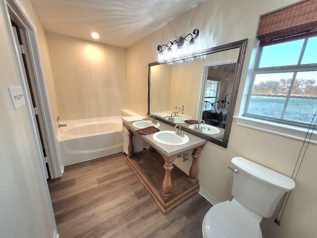 bathroom with toilet, dual sinks, hardwood / wood-style floors, and a tub