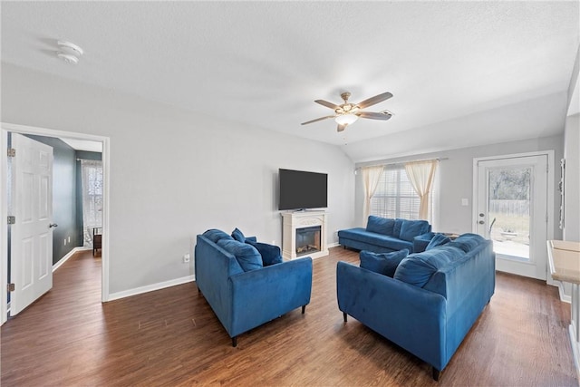 living area featuring baseboards, a ceiling fan, a glass covered fireplace, lofted ceiling, and wood finished floors