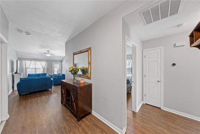 hall with baseboards, a textured ceiling, visible vents, and wood finished floors