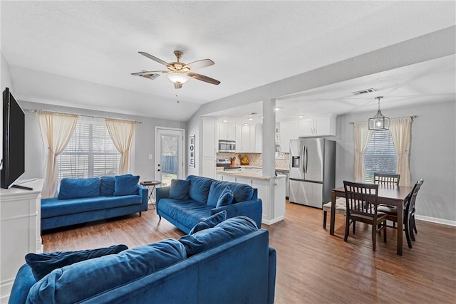 living area with vaulted ceiling, wood finished floors, and visible vents