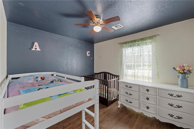 bedroom featuring a textured ceiling, a textured wall, wood finished floors, visible vents, and a ceiling fan