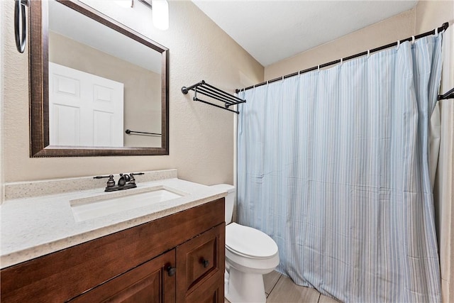 bathroom with a shower with curtain, a textured wall, vanity, and toilet