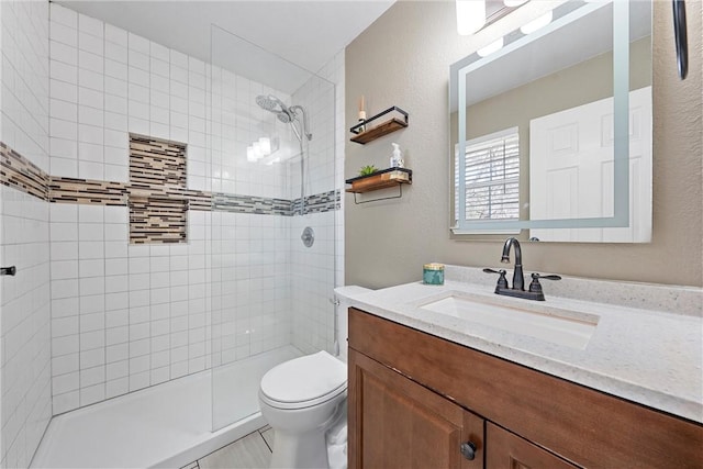 full bathroom with toilet, a textured wall, tiled shower, and vanity