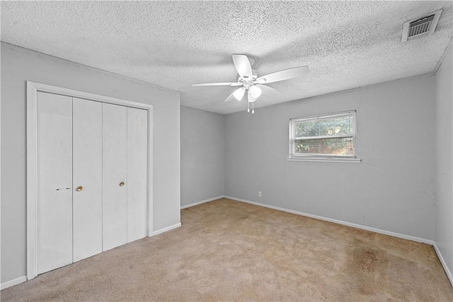 unfurnished bedroom with light carpet, a textured ceiling, a closet, and ceiling fan