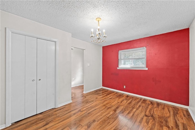 unfurnished bedroom with a chandelier, hardwood / wood-style floors, a textured ceiling, and a closet