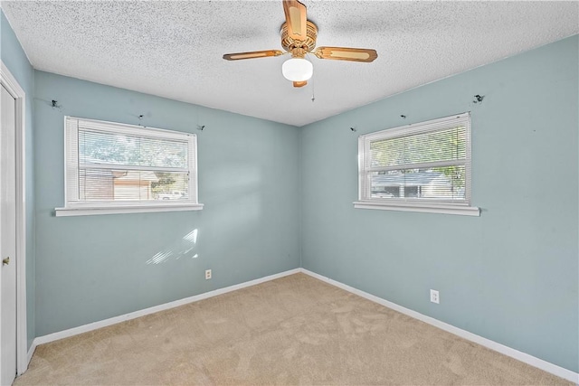 spare room featuring ceiling fan, light colored carpet, and a textured ceiling