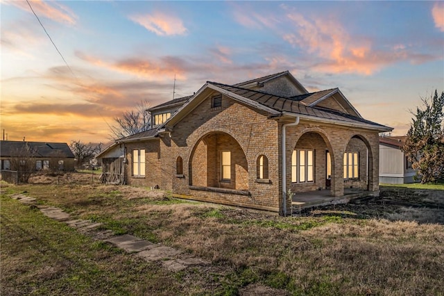 view of side of home featuring metal roof, brick siding, a standing seam roof, and a lawn