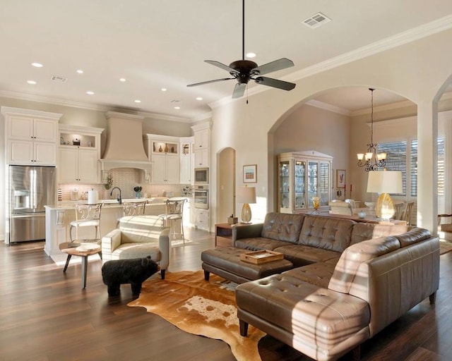 living room with dark wood-type flooring, ornamental molding, ceiling fan with notable chandelier, and sink