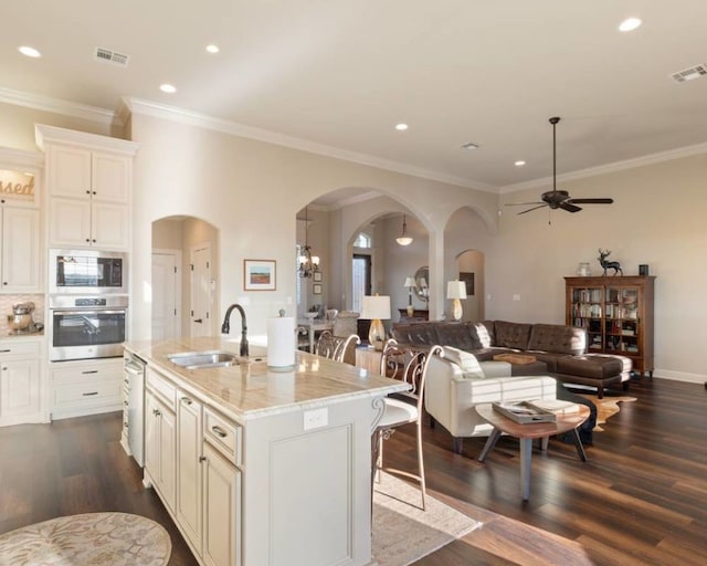 kitchen with a breakfast bar, an island with sink, sink, light stone counters, and stainless steel appliances