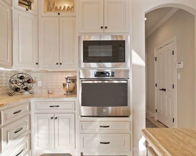 kitchen with white cabinetry, light stone counters, built in microwave, decorative backsplash, and oven