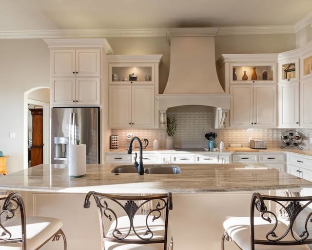 kitchen featuring sink, a center island with sink, a kitchen bar, stainless steel fridge with ice dispenser, and custom exhaust hood