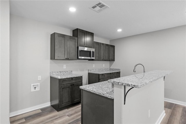 kitchen featuring a kitchen breakfast bar, light stone counters, a center island with sink, and light hardwood / wood-style flooring