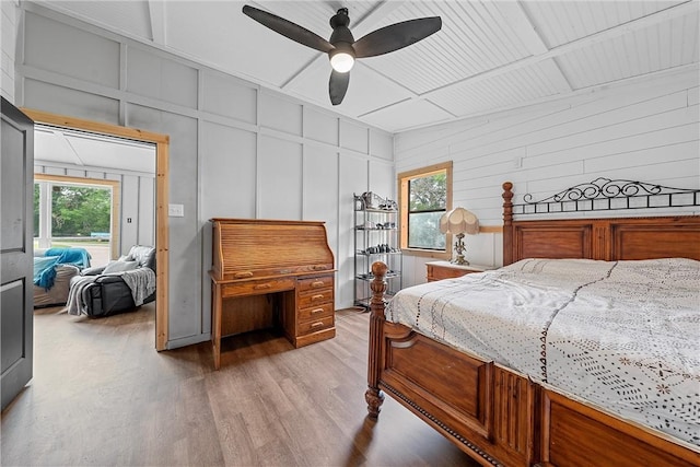 bedroom featuring multiple windows, light wood-type flooring, ceiling fan, and wood walls