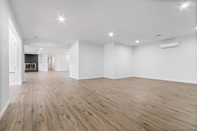 unfurnished living room with hardwood / wood-style flooring, a wall mounted AC, and a brick fireplace