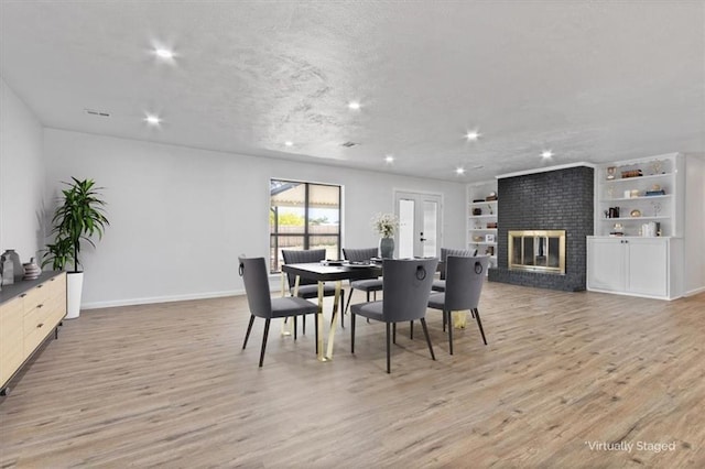 dining space featuring built in shelves, light hardwood / wood-style floors, a brick fireplace, a textured ceiling, and french doors