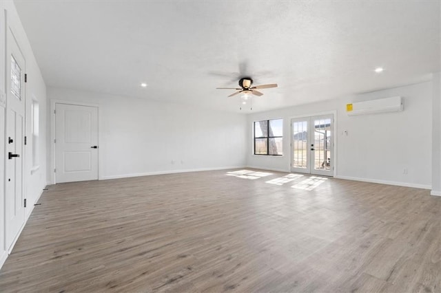 unfurnished living room with french doors, ceiling fan, a wall mounted air conditioner, and light wood-type flooring