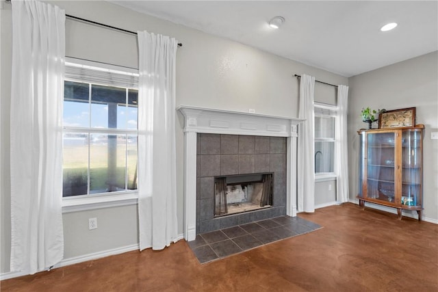 unfurnished living room with concrete flooring, recessed lighting, baseboards, and a tiled fireplace