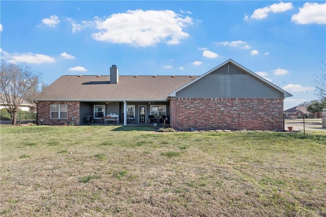 back of property with a patio, brick siding, a lawn, and a chimney