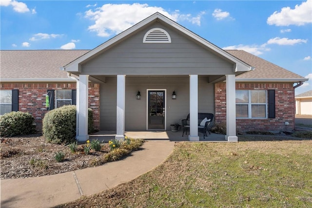 view of front of home featuring covered porch, brick siding, a front lawn, and a shingled roof