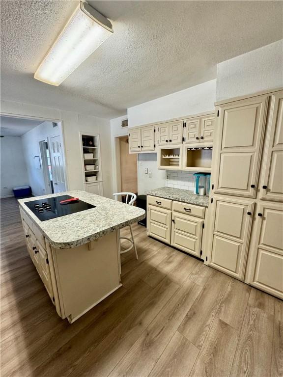 kitchen featuring cream cabinets, black electric cooktop, a breakfast bar, a kitchen island, and light wood-type flooring