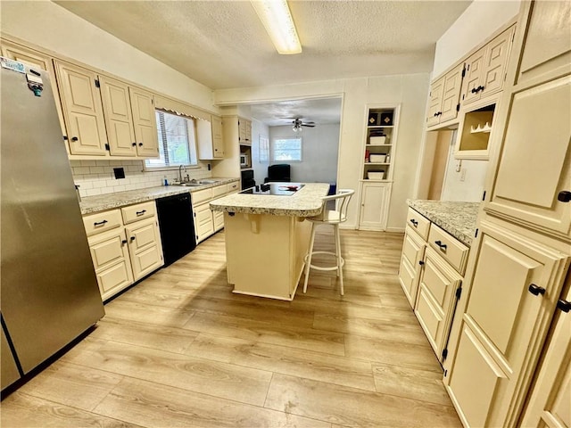 kitchen featuring light stone countertops, light hardwood / wood-style flooring, a kitchen bar, a kitchen island, and black appliances