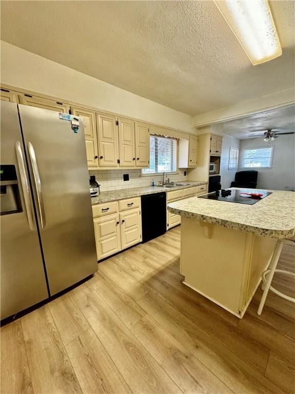 kitchen with a breakfast bar, light hardwood / wood-style floors, plenty of natural light, and black appliances