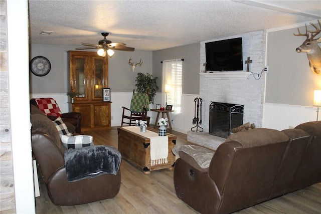 living room with ceiling fan, a fireplace, light hardwood / wood-style flooring, and a textured ceiling