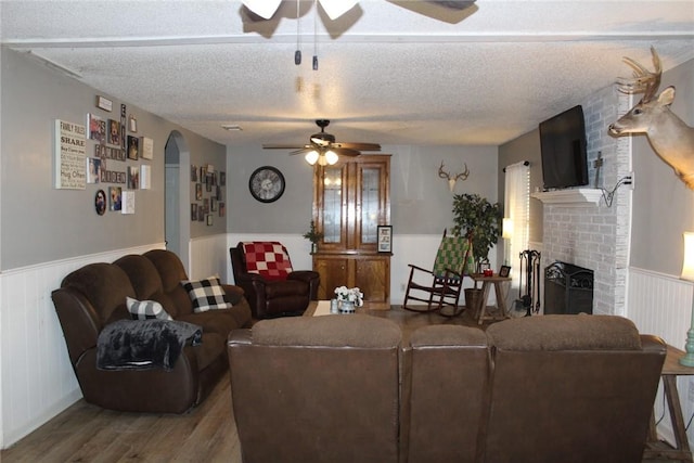 living room featuring ceiling fan, wood-type flooring, a brick fireplace, and a textured ceiling