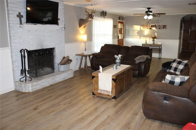 living room featuring crown molding, ceiling fan, wood-type flooring, and a brick fireplace