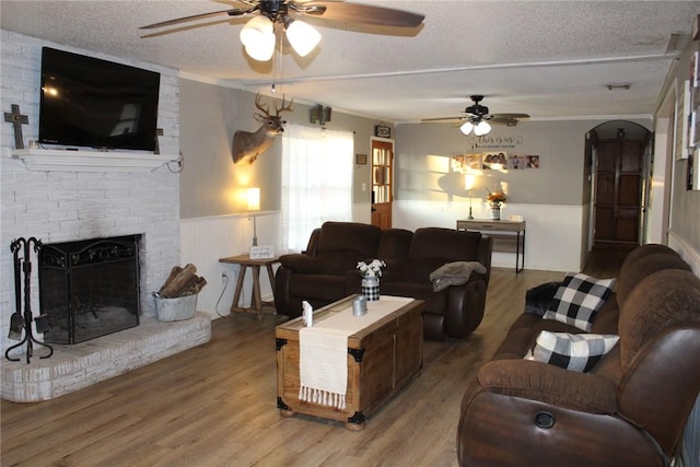 living room featuring hardwood / wood-style flooring, ceiling fan, a fireplace, and a textured ceiling