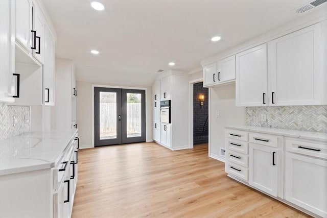 kitchen featuring light stone countertops, french doors, white cabinets, light hardwood / wood-style floors, and oven